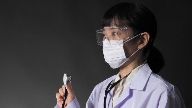 Doctor Wearing Medical Mask and clear goggles or glasses and stethoscope on the neck and white uniform. Asian female doctor or scientist in protective facial masks on black background. protect Covid 19 concept.
 

