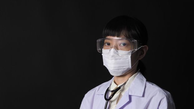 Doctor Wearing Medical Mask and clear goggles or glasses and stethoscope on the neck and white uniform. Asian female doctor or scientist in protective facial masks on black background. protect Covid 19 concept.
 
