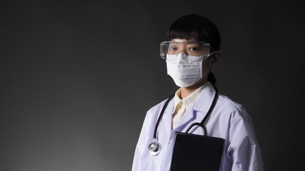 Doctor Wearing Medical Mask and clear goggles or glasses and stethoscope on the neck and white uniform. Asian female doctor or scientist in protective facial masks on black background. protect Covid 19 concept.
 
