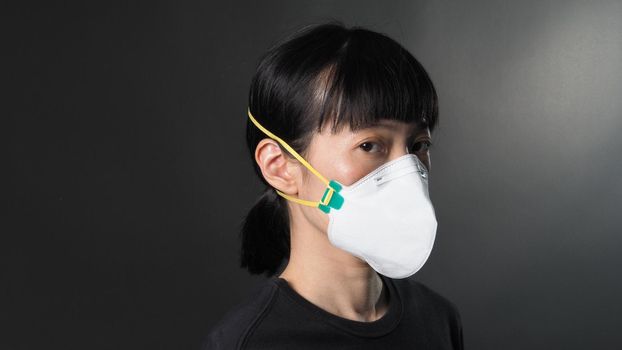 Asian girl in a mask on a black background in Coronavirus Quarantine situation. Title about the outbreak of the corona virus in the World, illness. Epidemic. female wearing N95 mask studio black background