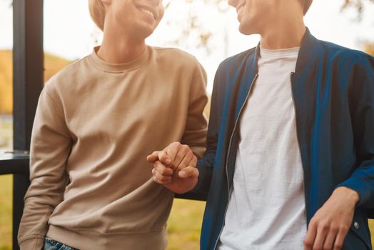 Cropped image of loving gay couple outdoors. Two handsome men having romantic date in park and holding hands. LGBT concept.