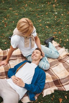 Loving gay couple having romantic date outdoors. Two handsome men sitting together on blanket in park. LGBT concept.