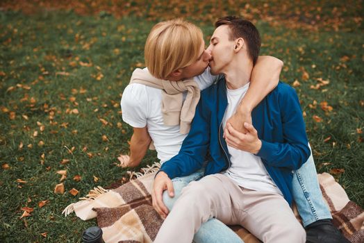 Loving gay couple having romantic date outdoors. Two handsome men sitting together on blanket in park and hugging. LGBT concept.