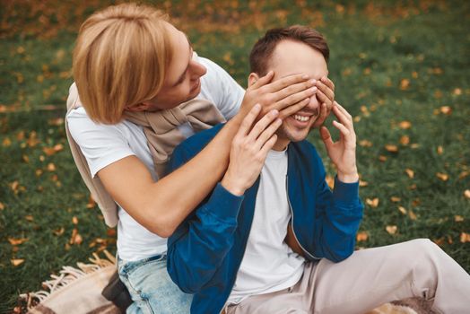 Loving gay couple having romantic date outdoors. Two handsome men sitting together on blanket in park. LGBT concept.