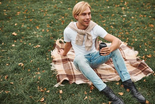 Handsome man having rest outdoors. Lying on blanket in park.