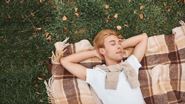 Handsome man having rest outdoors. Lying on blanket in park.