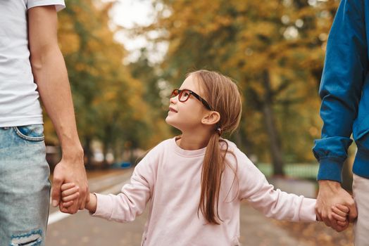 Cropped image of two gay parents with their adopted daughter holding hands and walking in park together. Happy LGBT family concept.