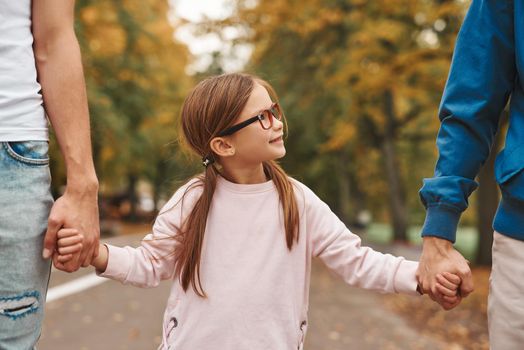 Cropped image of two gay parents with their adopted daughter holding hands and walking in park together. Happy LGBT family concept.