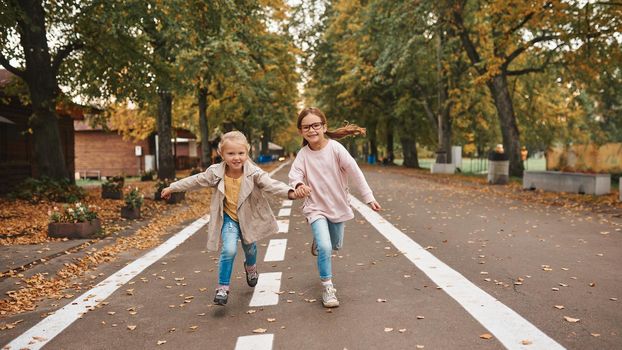 Two cute little girls having fun together and holding hands while running in park