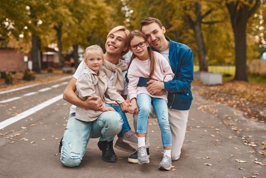 Two gay parents with their adopted daughters walking in park together. Happy LGBT family concept.