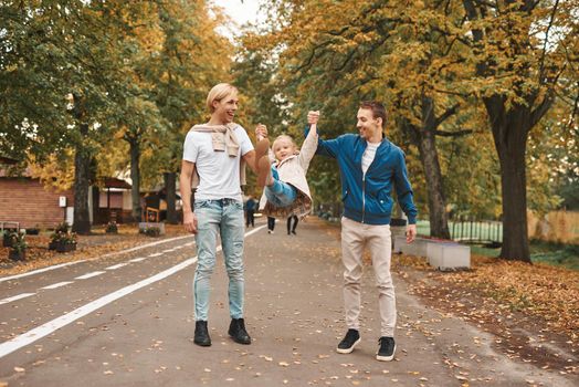 Two gay parents with their adopted daughter walking in park together. Happy LGBT family concept.