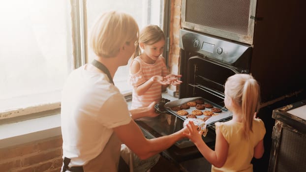Young father with two cute daughters cooking on kitchen. Family making cookies together at home.