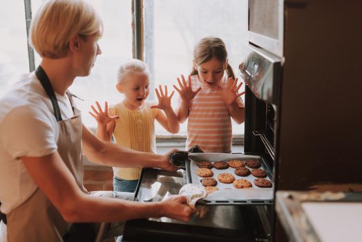 Young father with two cute daughters cooking on kitchen. Family making cookies together at home.