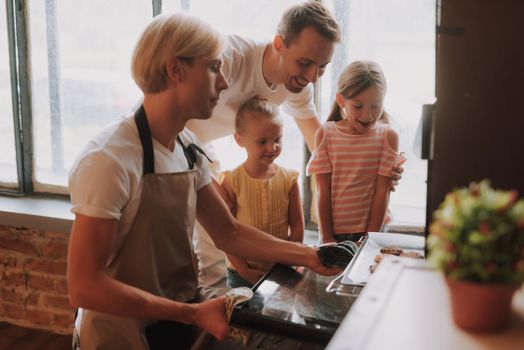 Gay couple with their adopted cute daughters cooking on kitchen. Lgbt family at home. Happy family making cookies together.