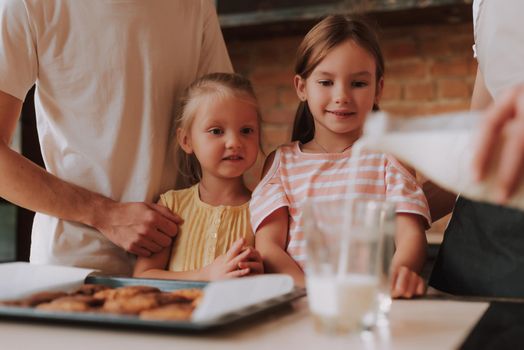 Cropped image of gay couple with their adopted cute daughters cooking on kitchen. Lgbt family at home. Portrait of two handsome men and their two little daughters eating cookies and drinking milk.