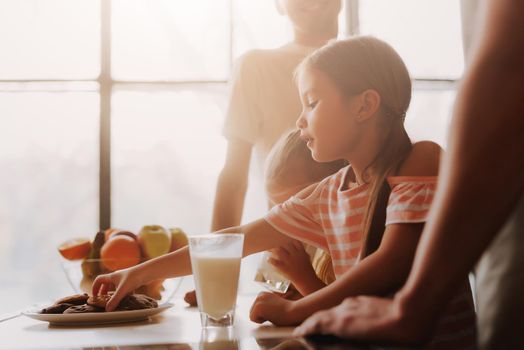 Cropped image of gay couple with their adopted cute daughters cooking on kitchen. Lgbt family at home. Small girl eating cookies and drinking milk.