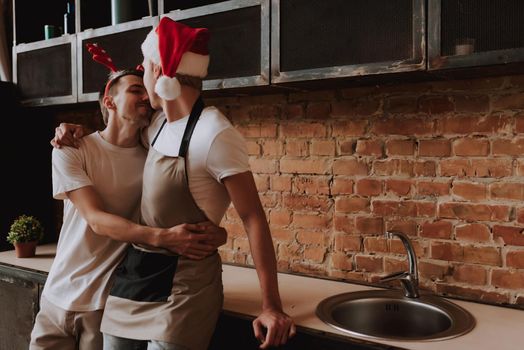 Loving gay couple at home. Two handsome men hugging and kissing on kitchen in Santa Claus hat. Christmas mood. LGBT concept.