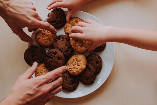 Top view image of adult and children hands taking cookies on the kitchen.
