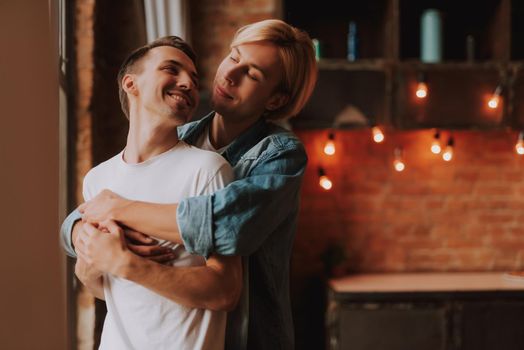 Loving gay couple at home. Two handsome men hugging and kissing on kitchen. LGBT concept.