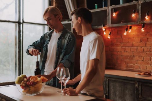 Loving gay couple at home. Two handsome men hugging and kissing on kitchen. Romantic atmosphere with bottle of red wine. LGBT concept.