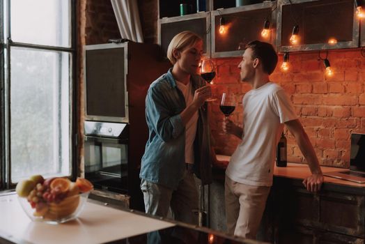 Loving gay couple at home. Two handsome men hugging and kissing on kitchen. Romantic atmosphere with bottle of red wine. LGBT concept.