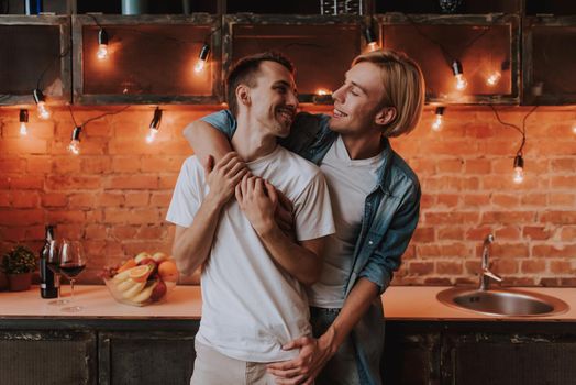 Loving gay couple at home. Two handsome men hugging and kissing on kitchen. LGBT concept.