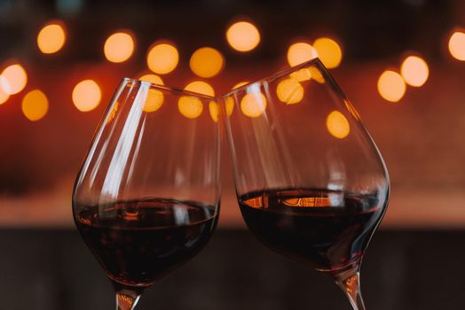 Cheers! Two wine glasses full of red wine on the background of romantic lights.