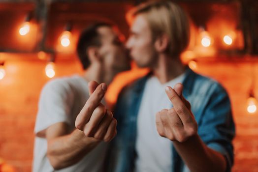 Loving gay couple at home. Two handsome men hugging and kissing on kitchen while showing sign love. LGBT concept.