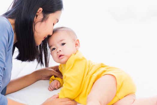 Portrait of beautiful young Asian mother kissing her infant newborn baby in a white bed, The mom loves his child, Healthcare and medical and mother day concept