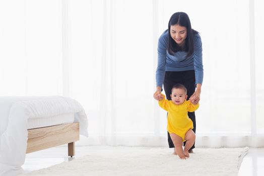 Asian little baby taking first steps learning to walk with mother help support the cute unstable walking toddler. Happy family first steps parenthood concept