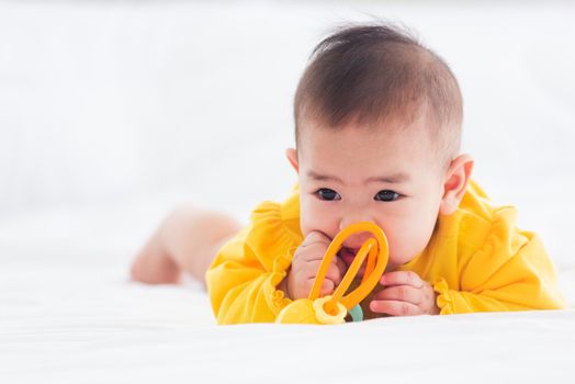 Portrait of beautiful young Asian newborn little baby prone on the bed at home, Happy baby smile wears a yellow shirt relaxing in the room, Family morning at home