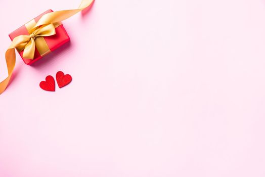 Happy Valentine's day composition background concept. Red gift box with a golden bow ribbon and wood red hearts for love isolated on pink background with copy space. Top View from above