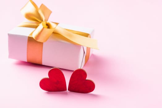 Valentines' day background concept. White gift box with a golden bow ribbon and wood red hearts composition greeting card for happy love isolated on pink background with copy space. View from above