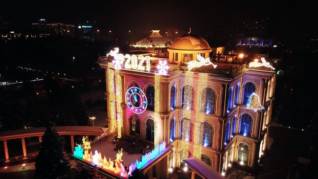 The city is decorated for Christmas and new year. Buildings, garlands, Christmas trees, fences and the square glow with different lights. People relax, enjoy the winter and holiday. View from a drone