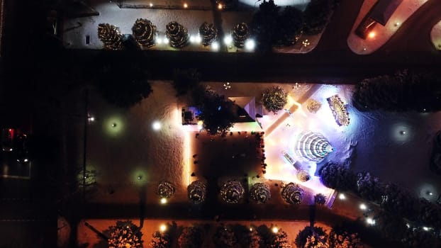 The city is decorated for Christmas and new year. Buildings, garlands, Christmas trees, fences and the square glow with different lights. People relax, enjoy the winter and holiday. View from a drone