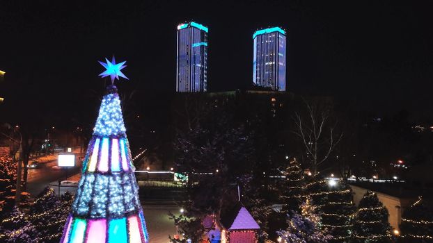 The city is decorated for Christmas and new year. Buildings, garlands, Christmas trees, fences and the square glow with different lights. People relax, enjoy the winter and holiday. View from a drone