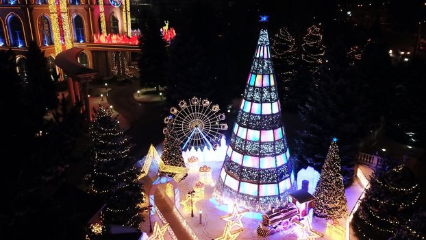 The city is decorated for Christmas and new year. Buildings, garlands, Christmas trees, fences and the square glow with different lights. People relax, enjoy the winter and holiday. View from a drone