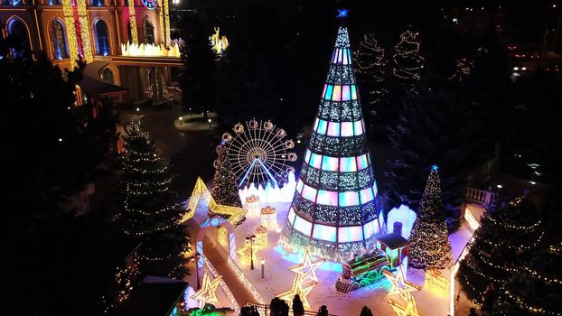 The city is decorated for Christmas and new year. Buildings, garlands, Christmas trees, fences and the square glow with different lights. People relax, enjoy the winter and holiday. View from a drone