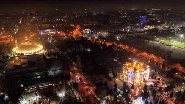 The city is decorated for Christmas and new year. Buildings, garlands, Christmas trees, fences and the square glow with different lights. People relax, enjoy the winter and holiday. View from a drone