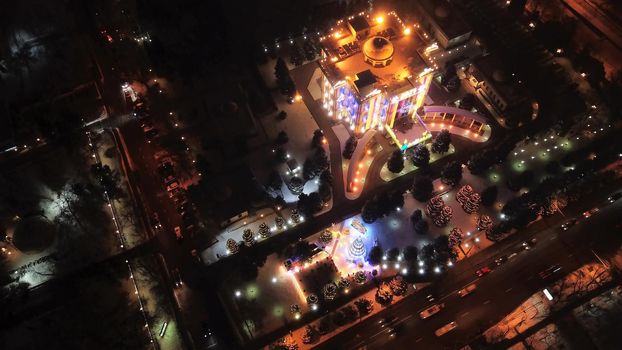 The city is decorated for Christmas and new year. Buildings, garlands, Christmas trees, fences and the square glow with different lights. People relax, enjoy the winter and holiday. View from a drone