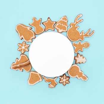 Christmas ornament with gingerbread cookies. Empty circle space for text and christmas cookies canvas around, flat lay or top view. Christmas baking on blue background