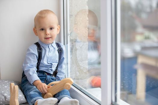 Little baby near the window. The kid with a toy sits on a window sill.Two year old child