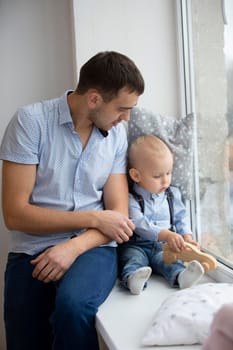 Father and little son are looking out the window. A man is playing with a child