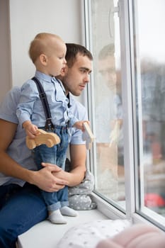 Father and little son are looking out the window. A man is playing with a child