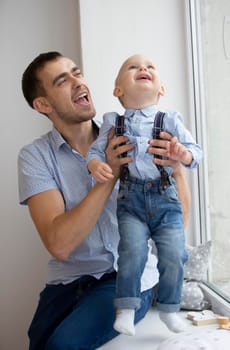 Happy father plays with the baby. A man with a small son near the window