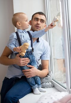 Father and little son are looking out the window. A man is playing with a child