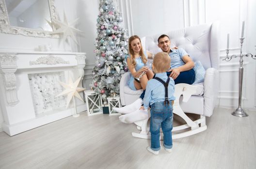 Family at Christmas. Mother father and child play against the background of a Christmas tree. Parents and son in the new year.