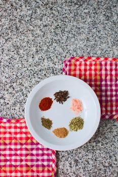 Ensemble of spices in a white dish over a granite countertop. Top down view.