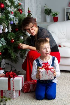 Son with mom at the Christmas tree. A child with a Christmas present.