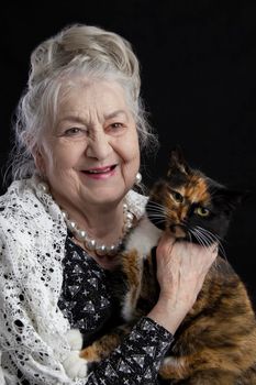 Portrait of a ninety year old woman with a pet. Merry old lady with a cat. Grandmother on a black background with a furry animal. Elderly beauty. The gray-haired well-groomed pensioner.